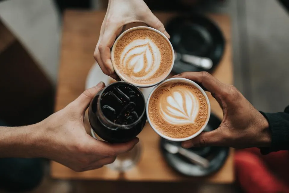Friends clinking flat whites over a cafe table