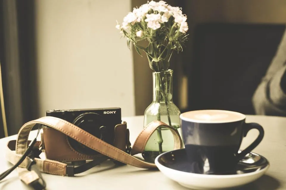 A flat white on a table beside a vase of flowers
